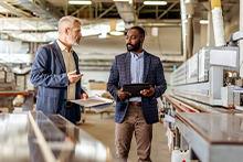 Two business men in a factory setting talking finances