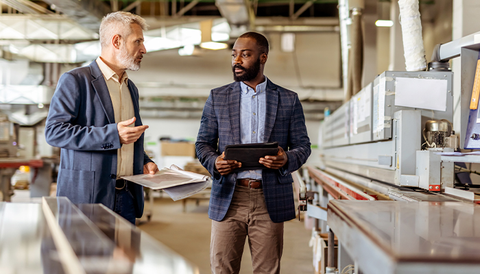 Two business men in a factory setting talking finances