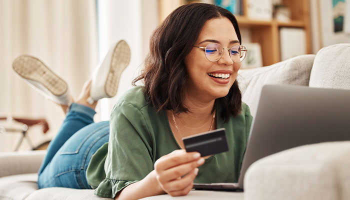 Young female laying on the couch with her debit card looking at online banking.