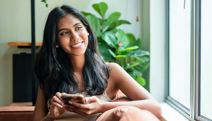 Young lady tracking her finances on her phone looking out a window