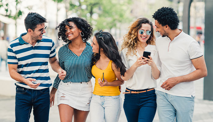 Group of diverse friends walking through town on their phones.