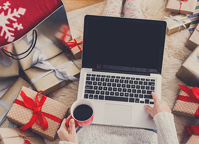 Depicted is a woman with a laptop holding coffee, surrounded by presents that are wrapped with a holiday theme