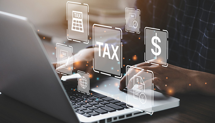 Person working on a laptop with TAX and MONEY icons floating above their hands.